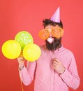 Hipster in giant sunglasses celebrating. Man with beard on cheerful face holds smiling mouth on stick, red background