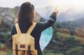 Hipster girl with backpack enjoying sunset on peak of foggy mountain, looking a map and poining hand. Tourist traveler on back Royalty Free Stock Photo