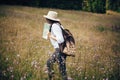 Hipster girl with backpack and map traveling in sunny mountains, walking in  wildflower meadow. Stylish happy woman in hat Royalty Free Stock Photo