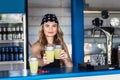 Hipster girl bartender serving fresh lemonade behind counter at outdoor bar