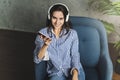 Hipster girl in earphones listening to music in online app sitting on sofa in her own apartment. Young lady downloading audio apps Royalty Free Stock Photo