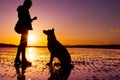 Hipster girl playing with dog at a beach during sunset, silhouettes