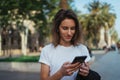 Hipster girl reads a nice text message on her mobile phone while standing in a Park on a warm summer day, gorgeous woman listens