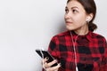 Hipster girl in red checked shirt having hair braided in a tail holding cell-phone listening to music or audiobook with headphones Royalty Free Stock Photo