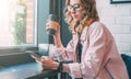 Hipster girl sitting in cafe at black table, drinking coffee and using smartphone. Businesswoman working online. Royalty Free Stock Photo