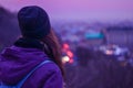 Hipster girl traveler looking at winter evening cityscape, purple sky and blurred city lights Royalty Free Stock Photo