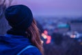 Hipster girl traveler looking at winter evening cityscape, violet sky and blurred city lights Royalty Free Stock Photo