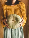 Hipster girl in yellow sweater holding pumpkins on rustic wooden background. Fall rural decor and arrangement. Autumn harvest.