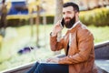 Hipster handsome young man sitting next to his laptop on the stairs while talking on his phone Royalty Free Stock Photo