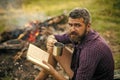 Hipster hiker with book and mug at bonfire on nature