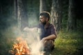 Hipster hiker with mug relax at bonfire in forest