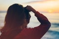 Hipster hiker tourist with backpack taking photo of amazing seascape sunset on camera on background blue sea, photographer enjoyin Royalty Free Stock Photo