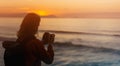 Hipster hiker tourist with backpack taking photo of amazing seascape sunset on camera on background blue sea, photographer enjoyin Royalty Free Stock Photo