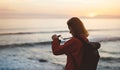 Hipster hiker tourist with backpack taking photo of amazing seascape sunset on camera on background blue sea, photographer enjoyin Royalty Free Stock Photo