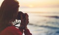 Hipster hiker tourist with backpack taking photo of amazing seascape sunset on camera on background blue sea, photographer enjoyin Royalty Free Stock Photo