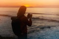 Hipster hiker tourist with backpack taking photo of amazing seascape sunset on camera on background blue sea, photographer enjoyin Royalty Free Stock Photo