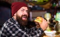 Hipster hungry man eat burger. Man with beard eat burger menu. Brutal hipster bearded man sit at bar counter. High