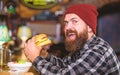 Hipster hungry man eat burger. Man with beard eat burger menu. Brutal hipster bearded man sit at bar counter. High