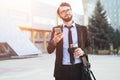 Hipster impressed businessman using smartphone on office build background with coffee thermo mug in hand and black bag.