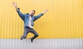 Hipster in a jeans jacket jumps against the backdrop of a bright yellow wall