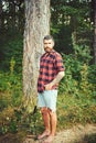 Hipster with long beard on natural green landscape. Bearded man with shovel in forest. Tourist in plaid shirt and jean Royalty Free Stock Photo