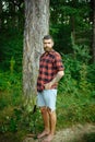 Hipster with long beard on natural green landscape. Bearded man with shovel in forest. Tourist in plaid shirt and jean Royalty Free Stock Photo