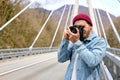 Hipster male in denim jacketwalking on bridge in countryside using camera