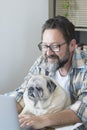 Hipster man with beard work at home on laptop computer and internet connection with his friend old dog together at the desktop - Royalty Free Stock Photo