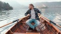 Hipster young man is paddling on the small boat in middle of magnificent lake at the background of the Alph mountains