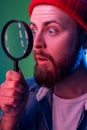 Hipster man standing, holding magnifying glass and looking aside and having astonished shocked face. Royalty Free Stock Photo