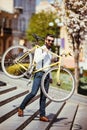 Hipster man in sunglasses carrying on his shoulder bike on street stairs. A young handsome man with beard holding bike on his righ Royalty Free Stock Photo