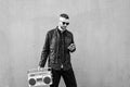 Hipster man using smartphone while listening music with a vintage boombox player against a wall background - Man wearing open face