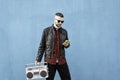 Hipster man using yellow smartphone while listening music with a vintage boombox player against a blue wall background - Man