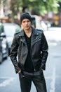 Hipster man wearing black style leather outfit with hat, pants, jacket and shoes standing on city street. Royalty Free Stock Photo