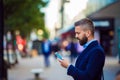 Hipster manager holding smartphone, texting outside in the street Royalty Free Stock Photo