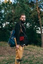 Hipster portrait brutal bearded and moustached woodcutter Gypsy man in the forest with ax. Travel style