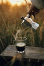 Hipster pouring fresh hot coffee from geyser coffee maker into glass cup in sunny warm light in rural countryside herbs.