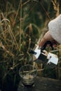 Hipster pouring fresh hot coffee from geyser coffee maker into glass cup in sunny warm light in rural countryside herbs.