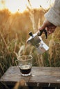 Hipster pouring fresh hot coffee from geyser coffee maker into glass cup in sunny warm light in rural countryside herbs.