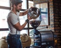 Hipster pouring raw coffee beans in a coffee roaster