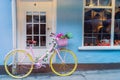 Hipster retro yellow bicycle with flower basket near old english style building with windows and doors with blue walls background Royalty Free Stock Photo