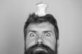 Hipster shocked face with apple stump target on head blue background, close up. Man handsome hipster long beard almost