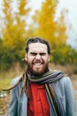 Hipster is smiling. A stylish man with dreadlocks and beard in a red shirt and grey jacket. Groom posing on nature