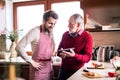 Hipster son with his senior father with tablet in the kitchen.