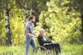 Hipster son walking with disabled father in wheelchair at park. Royalty Free Stock Photo