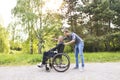 Hipster son walking with disabled father in wheelchair at park. Royalty Free Stock Photo