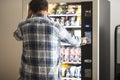 Hipster style man viewed from back buying snacks or drink from vending automatic machine typing product code. People and travel