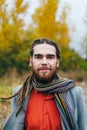 A stylish man with dreadlocks and beard in a red shirt and grey jacket. Groom posing on nature. Autumn wedding ceremony