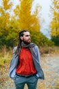 Hipster. A stylish man with dreadlocks and beard in a red shirt and grey jacket. Groom posing on nature. Autumn wedding