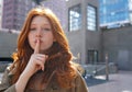 Hipster teen cool redhead fashion girl showing shh sign in city. Royalty Free Stock Photo